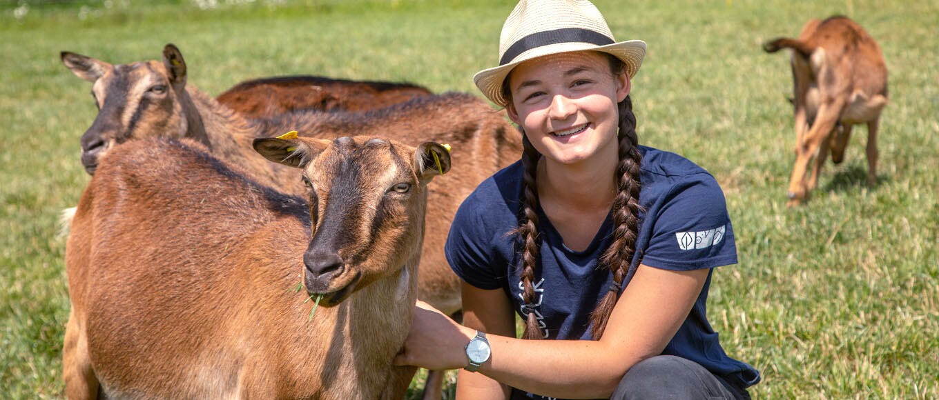 Teenagerin mit Stroh Fedora und zwei langen Zöpfen streichelt Ziegen