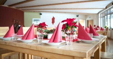 Ein festlich gedeckter Holztisch mit Gläsern, roten Servietten und Weihnachtssternen